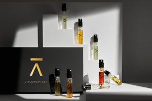 Image description: Azman Perfumes new discovery set photographed against a white background. The set features 8 fragrances, including the new Risk by Antonio Gardoni. The black hard box packaging has a flat opening and is adorned with a gold foil "A" from Azman and elegant lettering. 2ml vials on out from the box to show the range and depth.