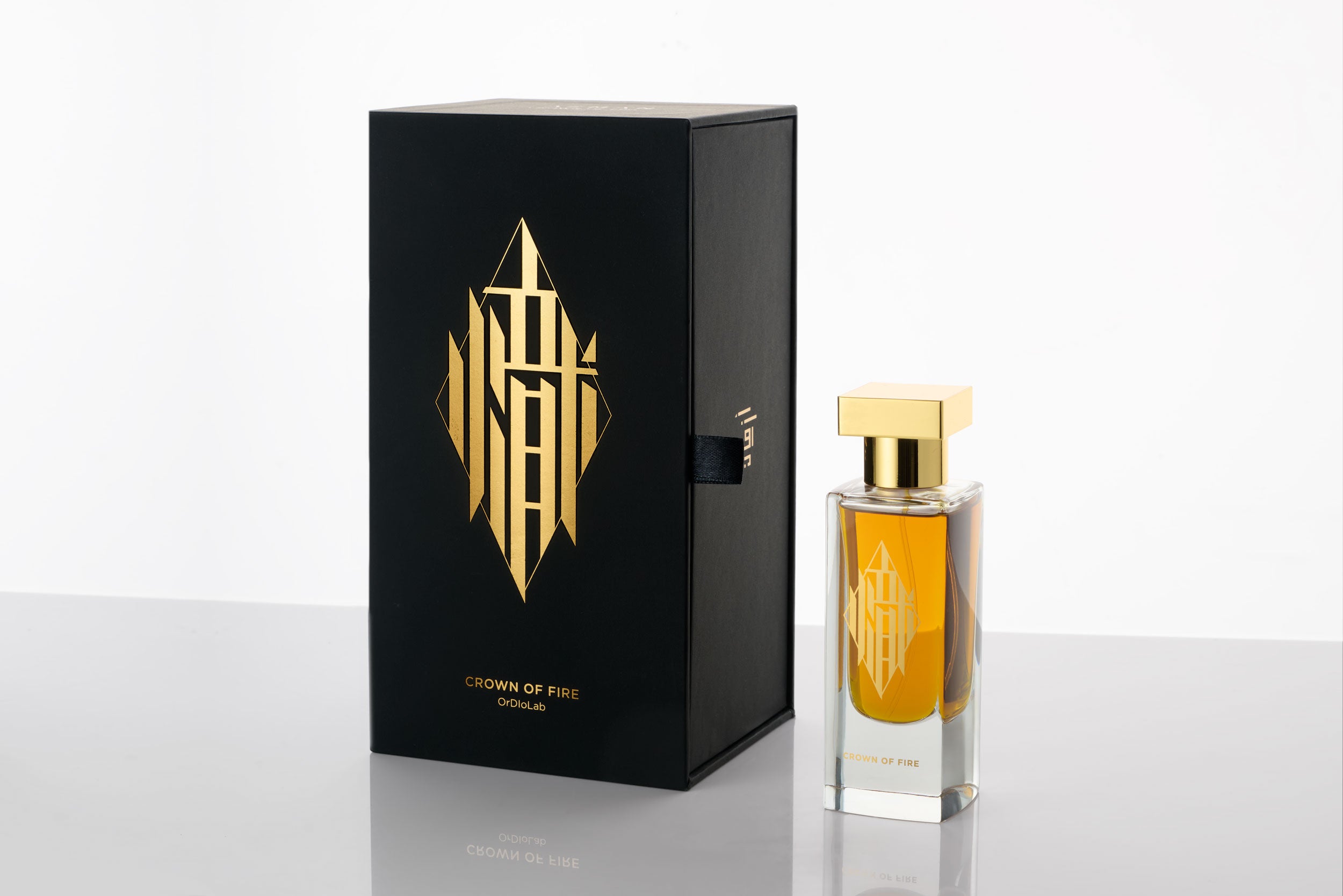 Perfume bottle labeled “Crown of Fire” with a gold cap, photographed on a white background and black box. The bottle features elegant Chinese calligraphy in 24 carat gold that translates to “fire.”